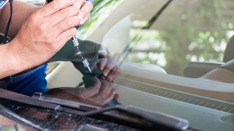 A person fixing a windshield on a car with a tool