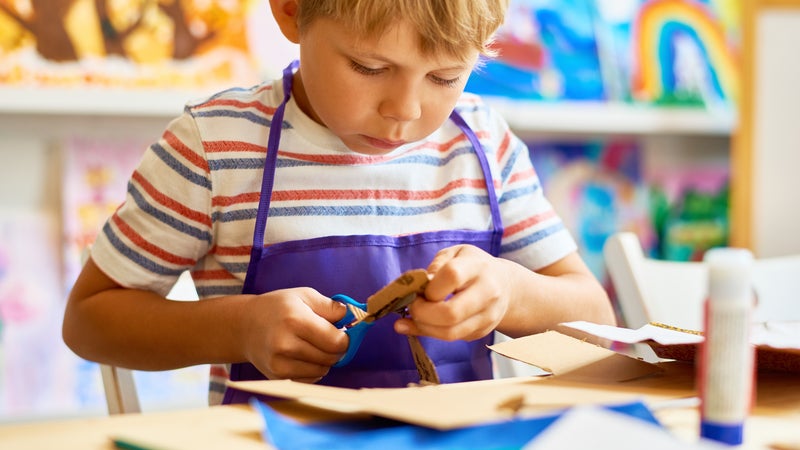 A child using scissors to cut cardboard in a classroom