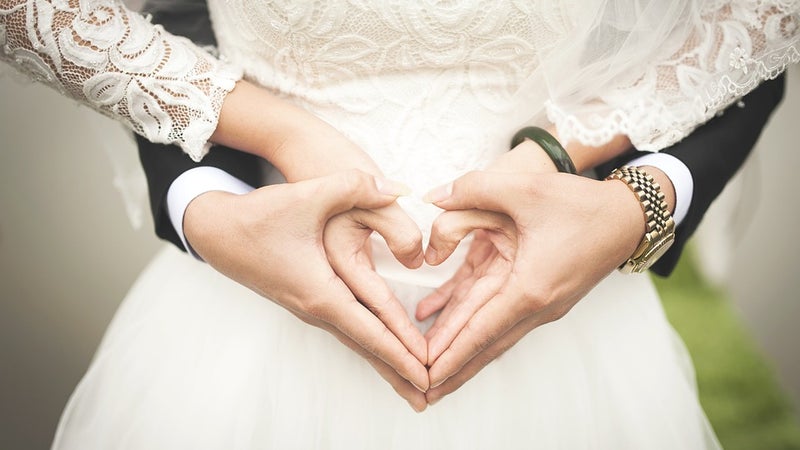 A couple's hands in the shape of a heart, wearing wedding attire