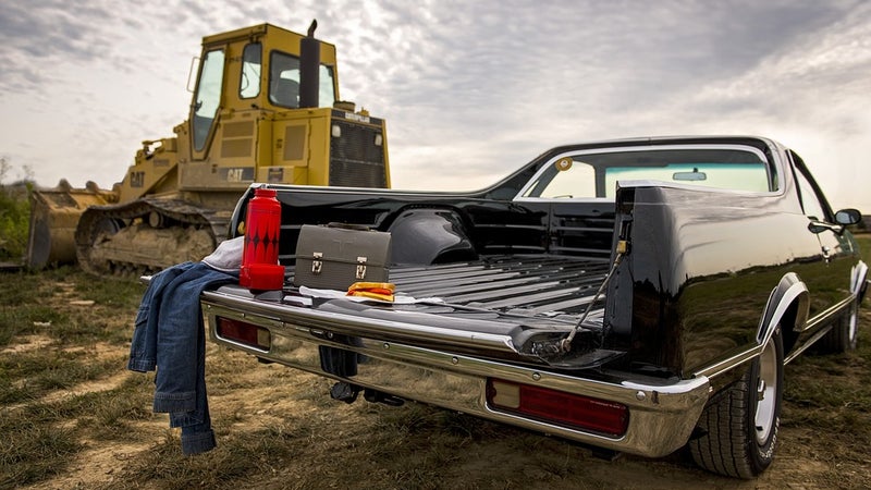 A black car with work supplies in the bed parked in front of a bulldozer
