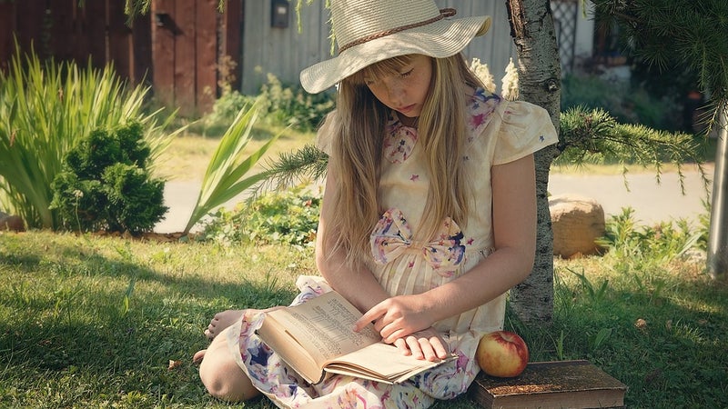 young girl sitting outside with a book
