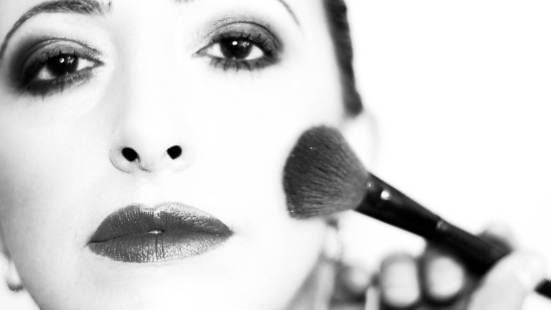 A black and white photo of a woman applying makeup