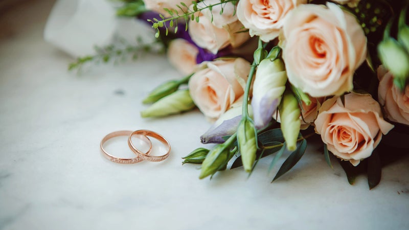 Two wedding bands on a marble surface next to a bouquet of flowers